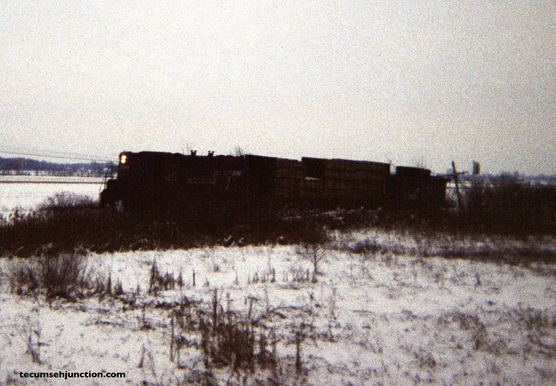 Having dropped off cars to the Lenawee County Railroad, the train heads north with just one car, here passing the approach signal to the N&W diamonds at Raisin Center, Michigan.. (12 December 1981)