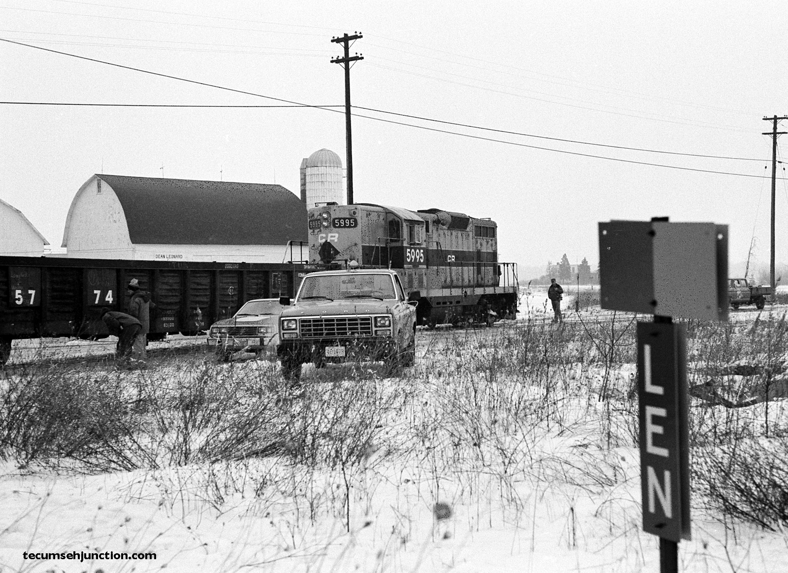 With the Lenawee Junction "LEN" block sign in the foreground, the train continues slowly backing across Deerfield Road.