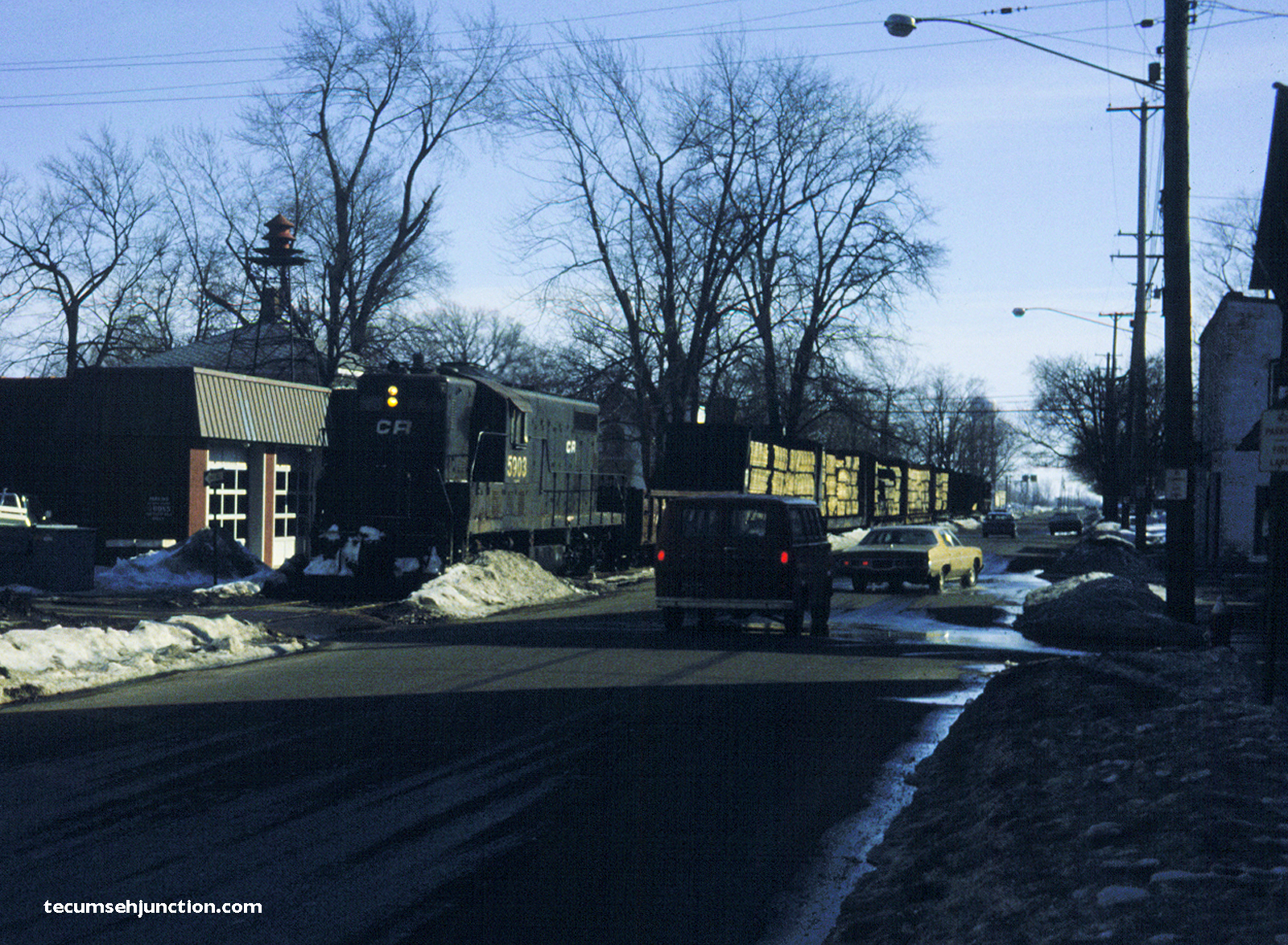 The train moves northward along S. Evans Street in Tecumseh, passing in front of the fire station.